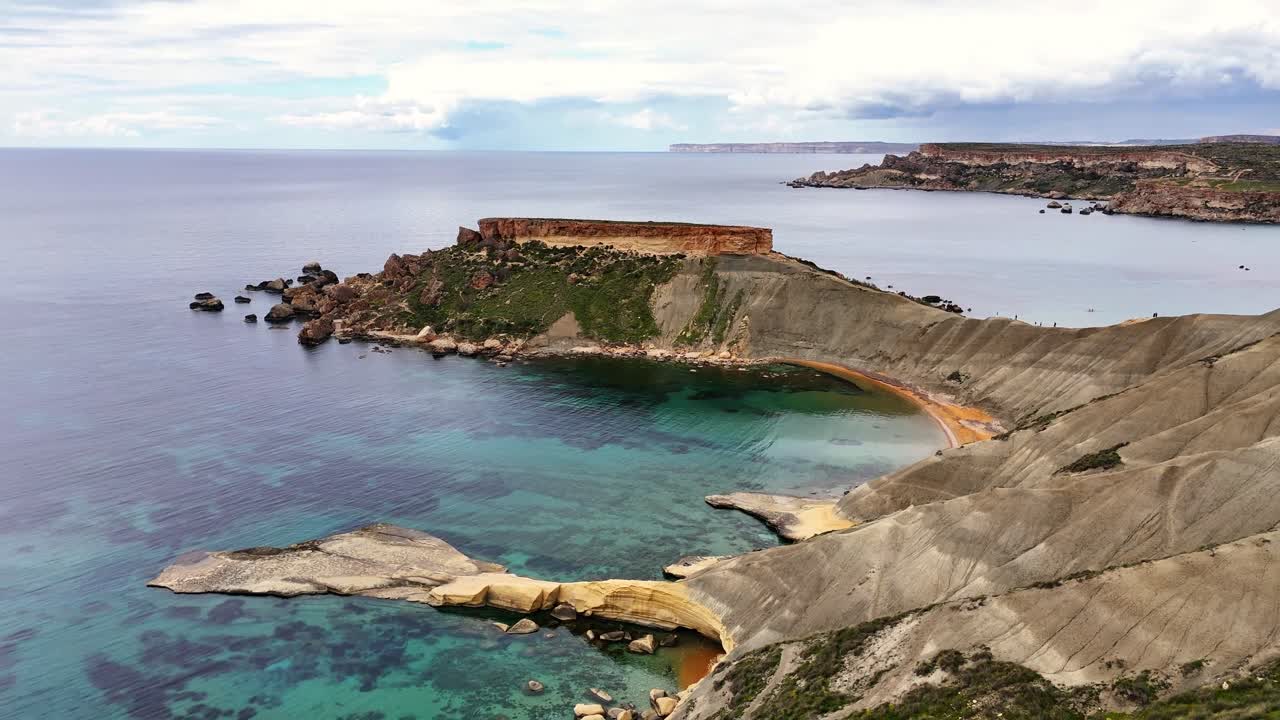 Vista aerea con drone di ripide scogliere costiere e un'insenatura curva a Qarraba Bay, Malta, con acqua turchese limpida, costa rocciosa e terreno in pendenza alla luce naturale del giorno.