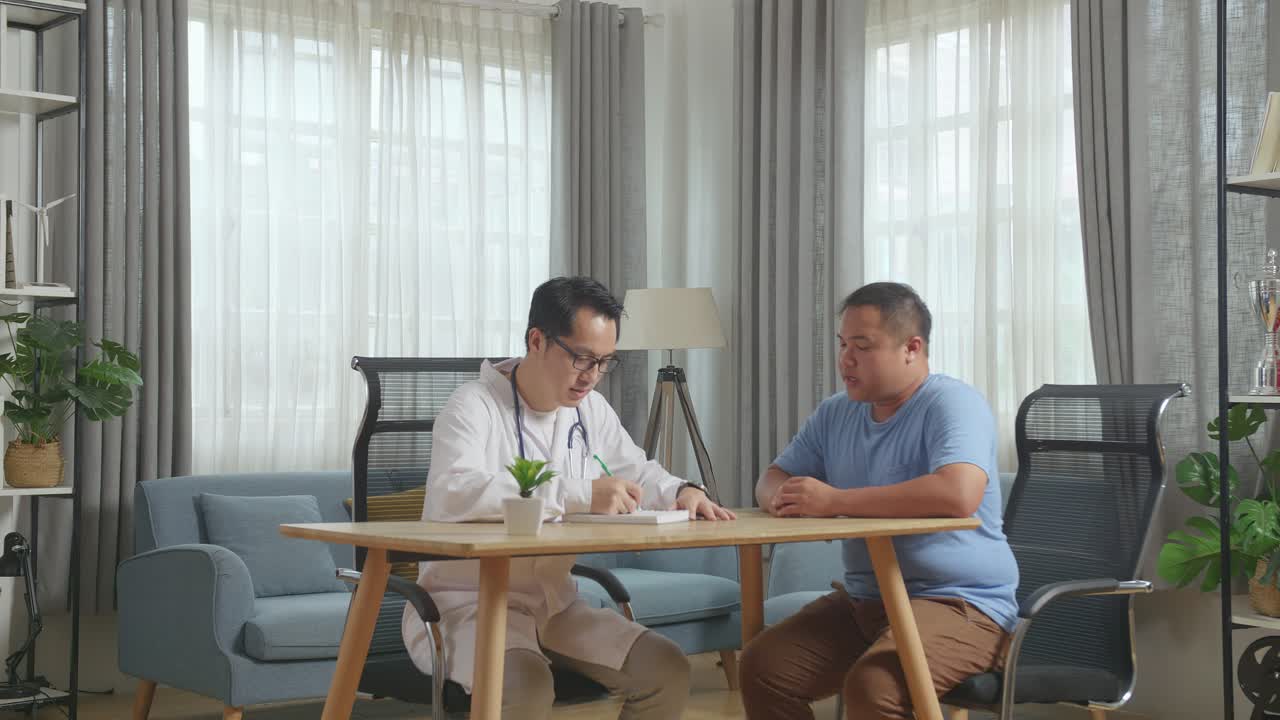클리닉에서 한 남성 환자와 함께 책상에 앉아 환자에게 처방전을 쓰고 이야기하는 아시아 남성 의사