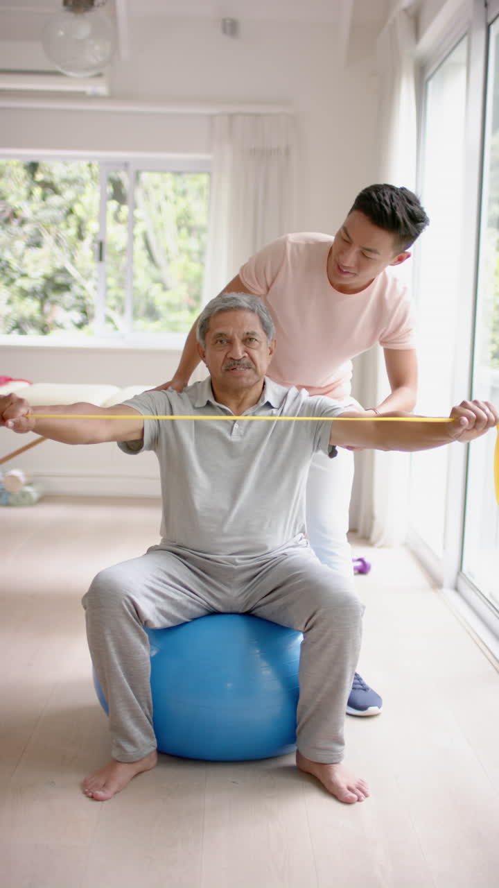Vertical video of diverse male physiotherapist and senior male patient exercising, in slow motion