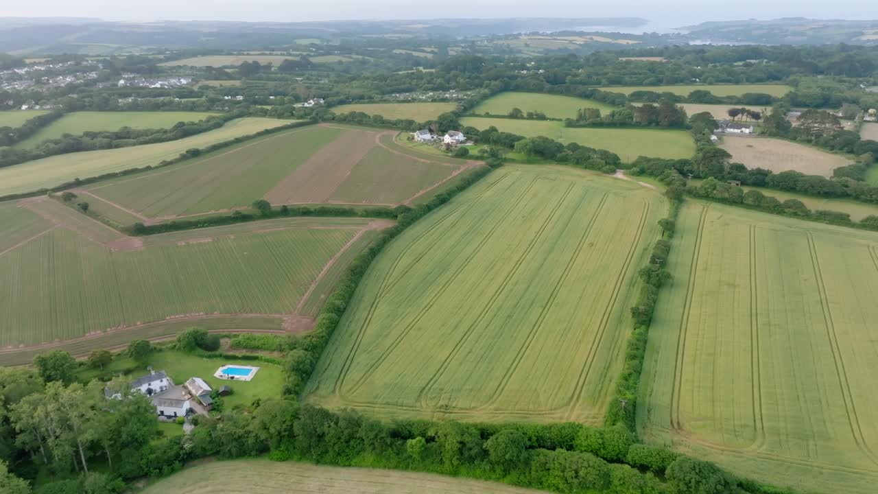 Farmhouse with swimming pool amongst patchwork fields lined by hedgerows. Summer, Cornwall, UK.
