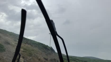 shot from car of big wind turbine over green mountains under cloudy sky, rainy weather