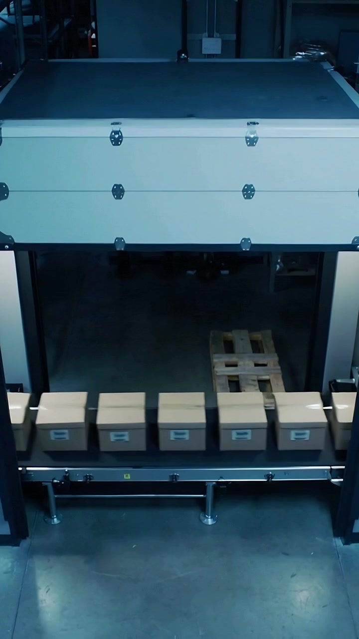 Vertical video: Lowering overhead hood on conveyor in plant as six boxes entering covering packages