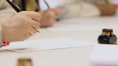 group-of-peoples-hand-writting-oldschool-black-ink-pen-on-the-white-sheet-of-paper-close-up-slow-motion