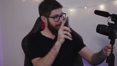 un hombre adulto con barba está grabando un video como un blogger sosteniendo y hablando con una cámara profesional en casa