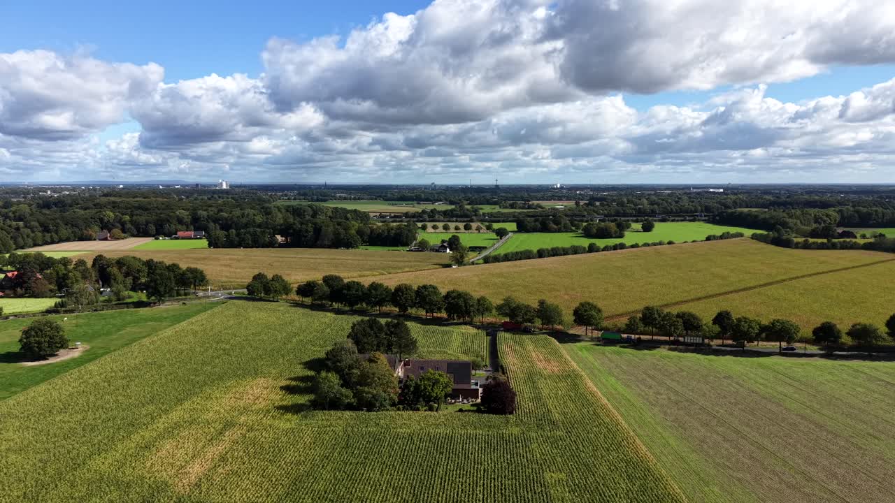 Countryside scene in rural district of town. Late summer day with cultivated fields and driving tractor and trailer at work. Aerial wide shot. Farmstead house with solar panels on roof in America