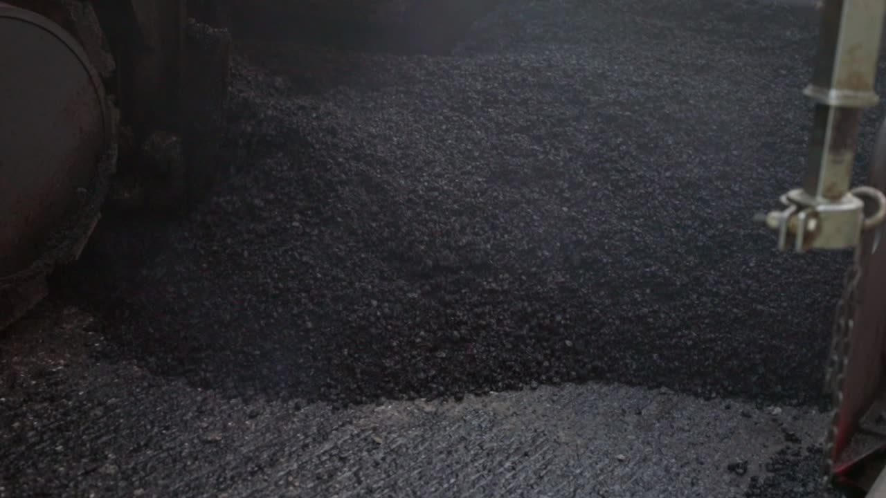 Asfalto fresco da distribuire a terra per la costruzione di strade, vista frontale da un'angolazione bassa, Slow Motion.