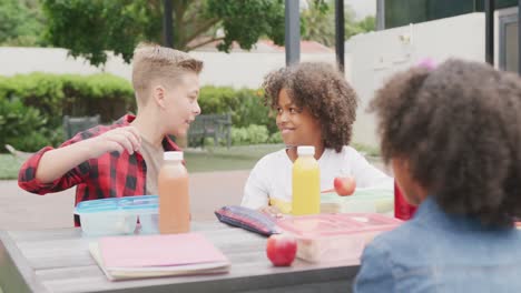 video of three diverse schoolchildren talking at lunch sitting in schoolyard