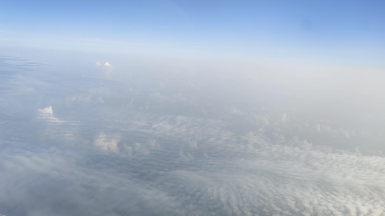 A serene stretch of sky frames textured clouds below, captured from a cruising altitude, offering a tranquil glimpse of nature’s beauty in motion