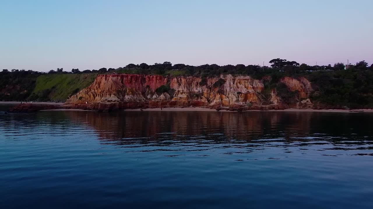 A dynamic shot moving towards the Red Bluff cliffs, highlighting their rugged beauty and striking rock formations against the backdrop of the ocean.