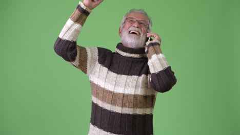handsome senior bearded man wearing warm clothing against green background