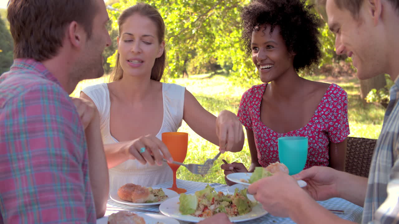 cuatro amigos comiendo juntos en una mesa al aire libre