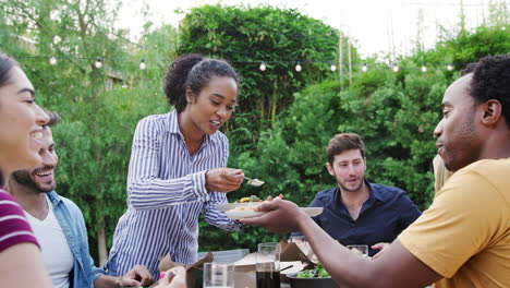 woman serving group of multi-cultural friends at home at table enjoying food at summer garden party