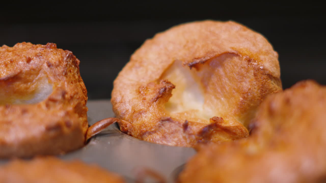 Paneo a través de pequeños pudines Yorkshire ingleses recién cocinados con luz cenital. Perfecto para anuncios de comida de alta gama, promociones de asado dominical británico y encabezados de recetas apetitosas.