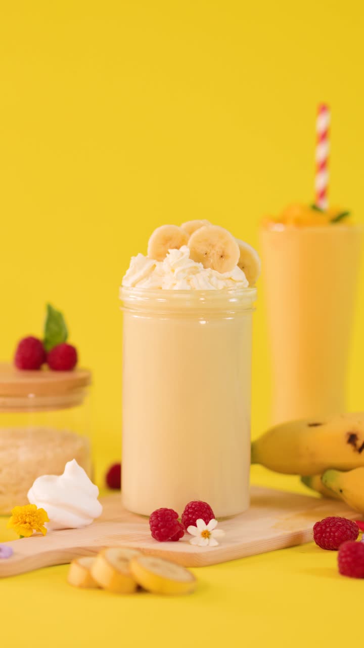 Primo piano di un frullato di banana guarnito con panna montata e frutta su uno sfondo giallo brillante.