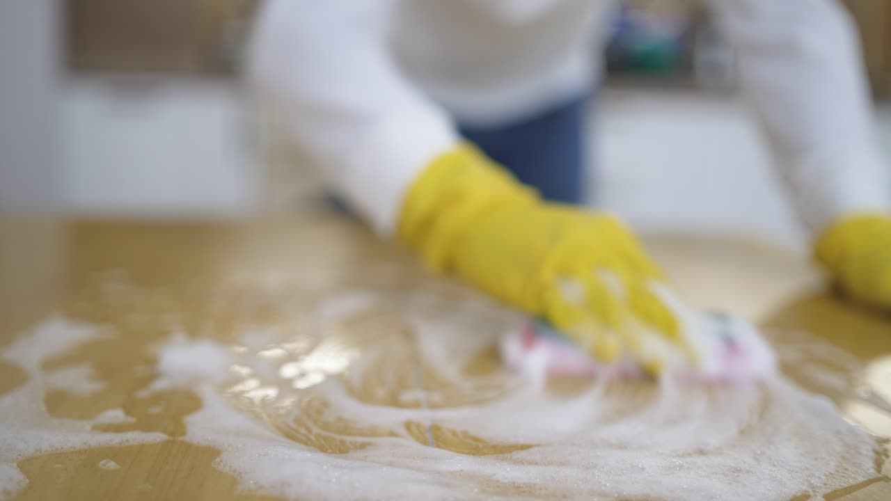 Man cleans a table using a sponge with visible foam while performing spring cleaning, highlighting household chores, hygiene, home maintenance, and domestic cleaning routine in a tidy indoor environme