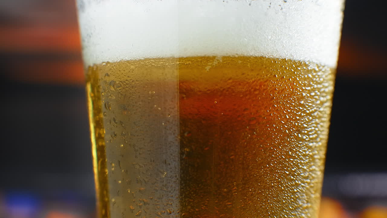 close-up cámara lenta: cerveza fría en un vaso grandes gotas y burbujas en la cerveza