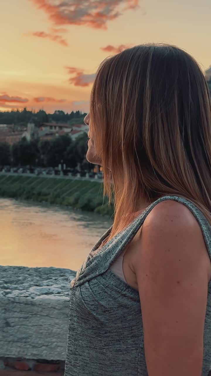 Pensive woman watching the sun setting over the water with a city in the background