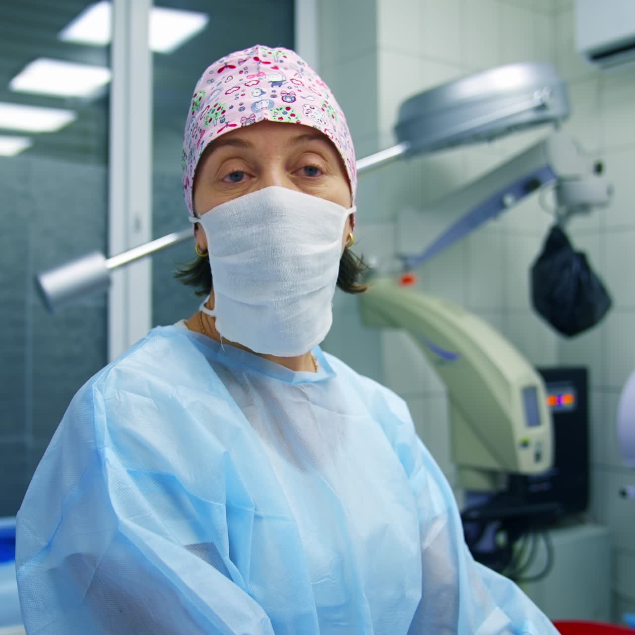 Doctor in scrubs and facial mask tells methods of vision correction to the camera. Modern clinic background