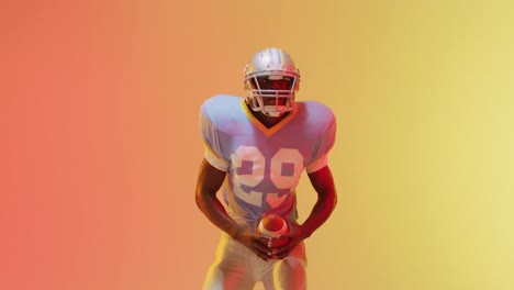 Video-of-african-american-american-football-player-with-ball-over-yellow-to-orange-background