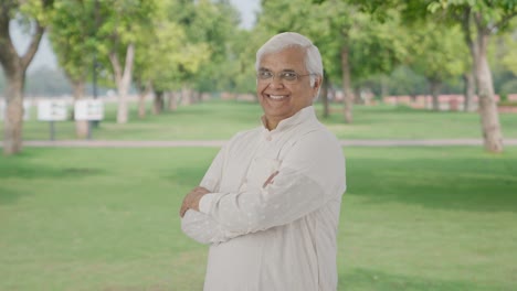 Portrait-of-Happy-Indian-old-man-standing-crossed-hands-in-park