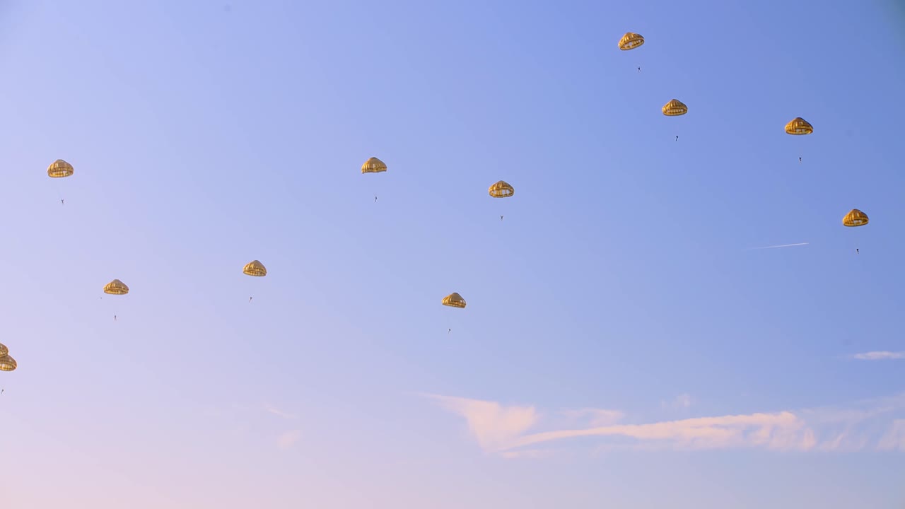 황금색 낙하산에 탑승한 여러 낙하산은 밝은 파란 하늘을 향해 느슨한 포메이션으로 내려갑니다.