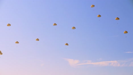 varios paracaidistas en paracaídas dorados descendiendo en formación suelta contra un cielo azul brillante
