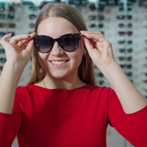 pretty girl buying new sunglasses. beautiful smiling young woman tries on stylish glasses and admires herself in the optical store. summer look.