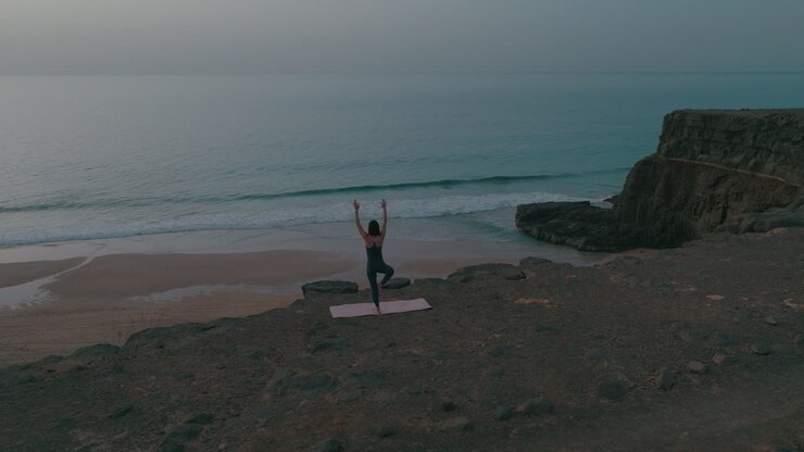 Woman practicing yoga on a beach cliff overlooking the ocean