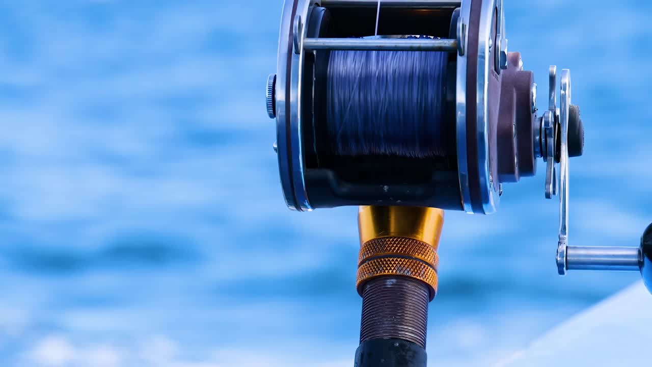 Detailed view of a fishing reel with a blurred ocean background, highlighting the equipment's metallic and plastic components.