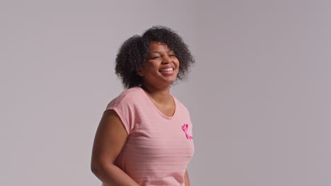 studio portrait of smiling mid adult woman wearing pink breast cancer awareness ribbon against white background