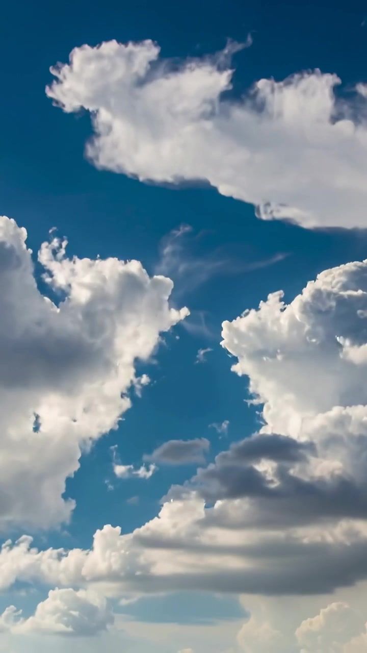 Video verticale: Massa di nuvole convettive alla deriva che apre una fessura centrale nel cielo, con filamenti che si assottigliano e cime illuminate.