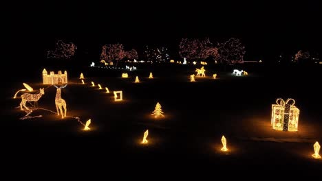 Eine-Drohnenaufnahme-Eines-Winterwunderlandes-Mit-Festlichen-Weihnachtslichtern,-Hirschen,-Geschenkboxen-Und-Immergrünen-Bäumen