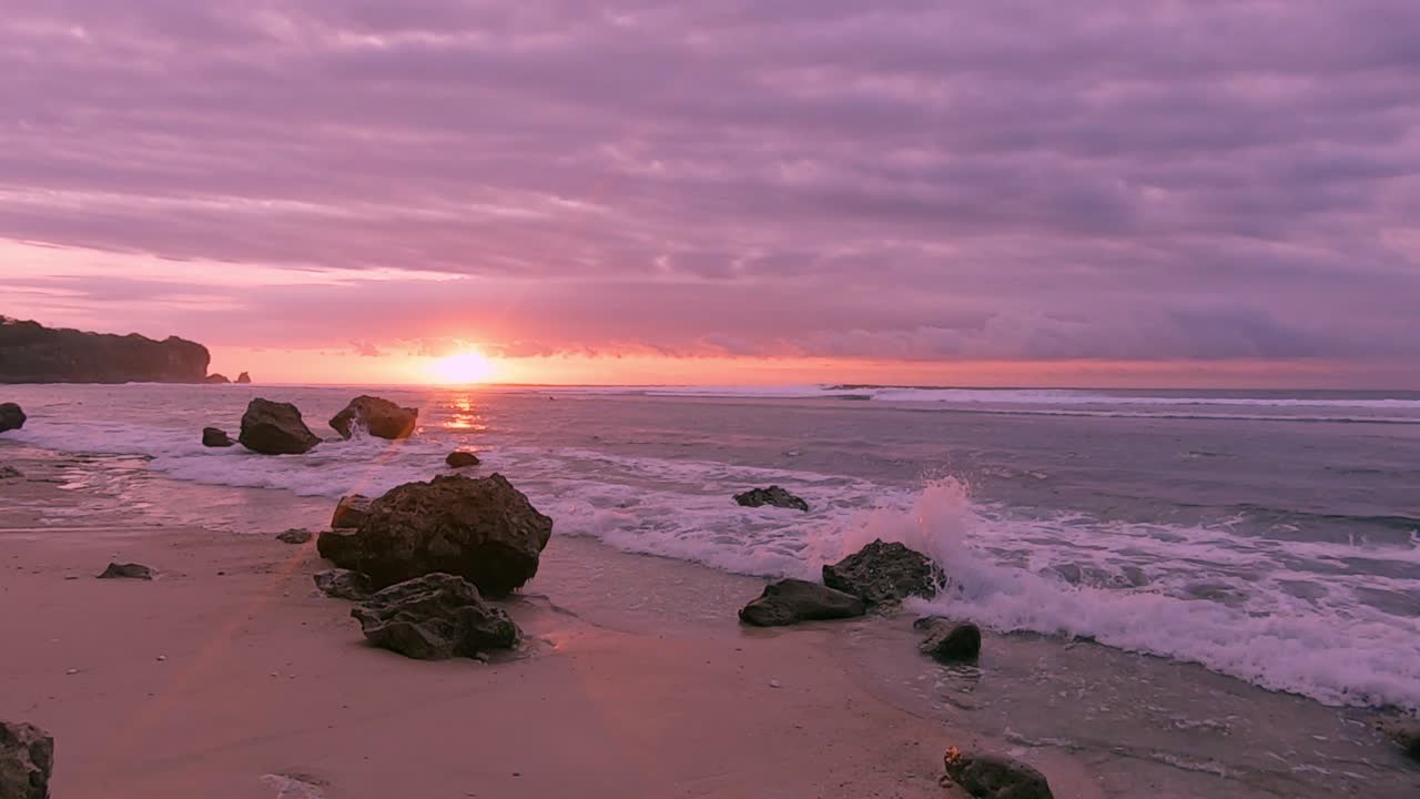 puesta de sol debajo de nubes coloridas en una tranquila playa rocosa en bali
