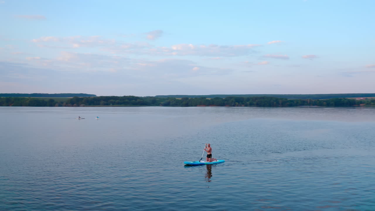 Man sails on boat at sunset. Silhouette of a man rowing on a board on evening water on the background of industrial factory near the river. Extreme sport on water concept