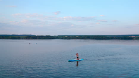 man sails on boat at sunset. silhouette of a man rowing on a board on evening water on the background of industrial factory near the river. extreme sport on water concept