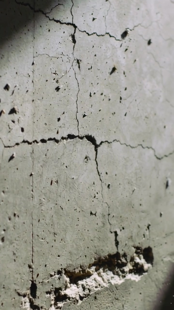 Video verticale: Telecamera che esegue una panoramica ispezionando una parete di cemento intonacata all'interno, rivelando una scanalatura scheggiata.