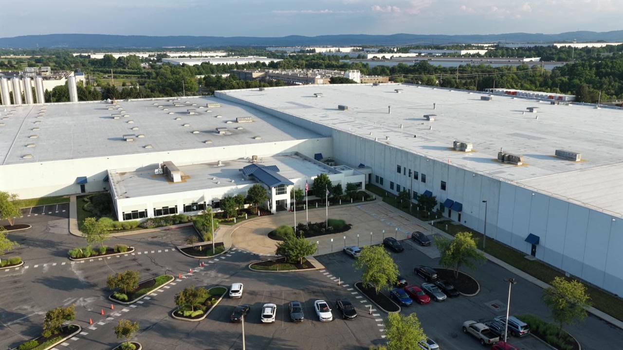 Hvidt industrilager strækker sig over en stor distributionspark med flade tagmonterede HVAC-enheder, anlagt indgang og parkeringsplads omgiver anlægget nær Allentown, Pennsylvania. Luftfoto drone vidvinkeloptagelse i kredsløb
