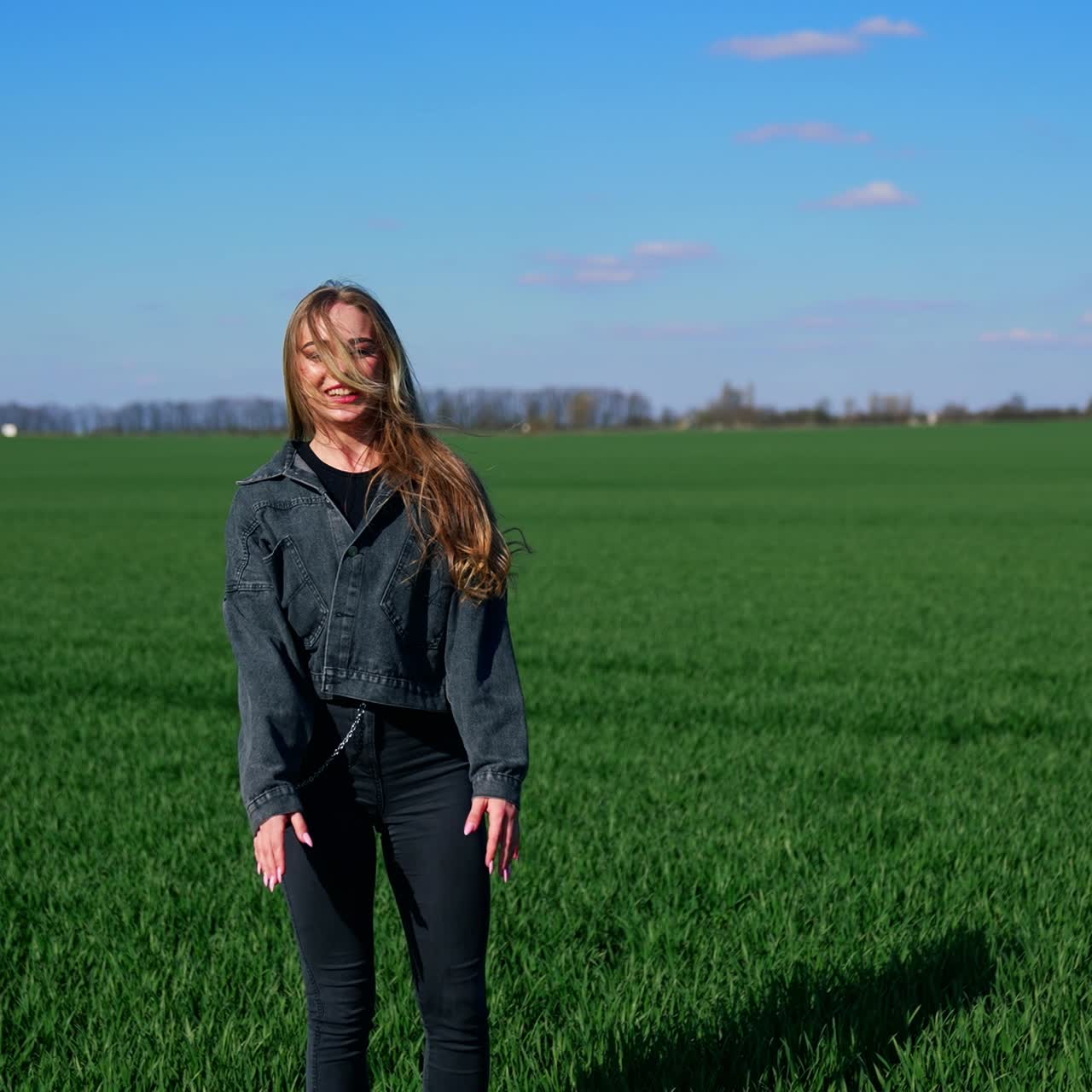 Fröhliches Mädchen auf einer grünen Wiese. Schöne junge Frau in Jeanskleidung genießt die Natur im Frühling. Attraktive Frau springt fröhlich auf einer Wiese.