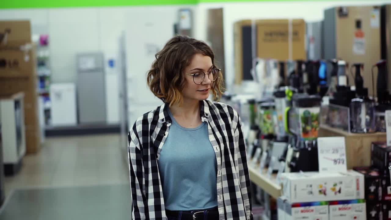 seguimiento de imágenes de vista frontal de una niña con una camisa a cuadros y cabello rizado corto caminando por el supermercado en electrodomésticos