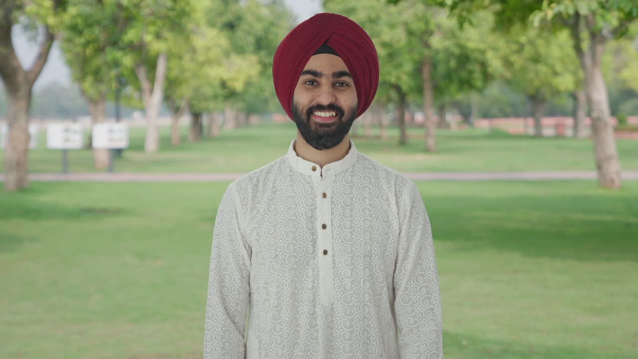 Uomo indiano sikh sorridente alla telecamera in un parco