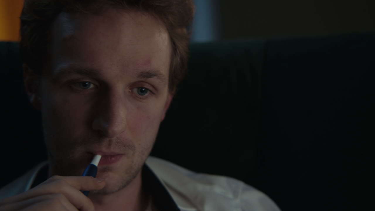Close-up of a man smoking a vape pen, looking pensive