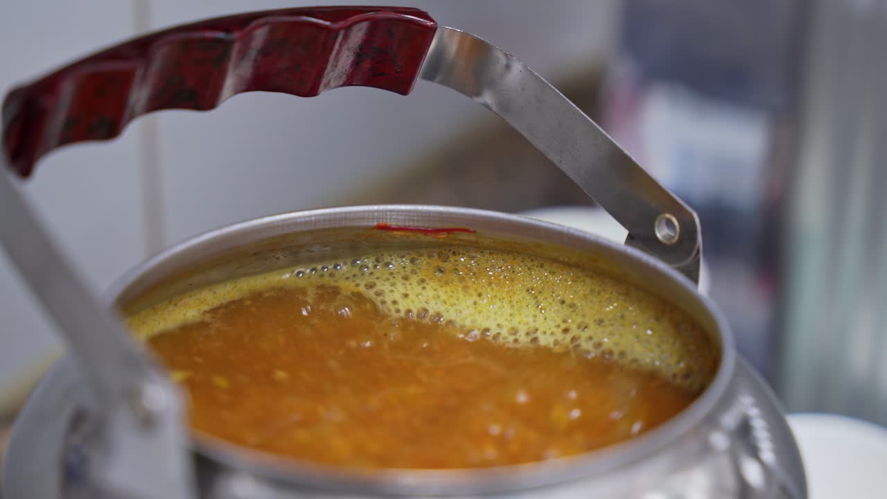 Caffè arabo tradizionale che bolle in una caffettiera d'argento con manico rosso. Zafferano e spezie creano schiuma gialla sulla superficie durante la preparazione in una cucina luminosa
