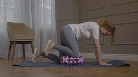 mujeres caucásicas colocando la rodilla en la almohada en la alfombra de yoga y levantando la pierna izquierda en el aire