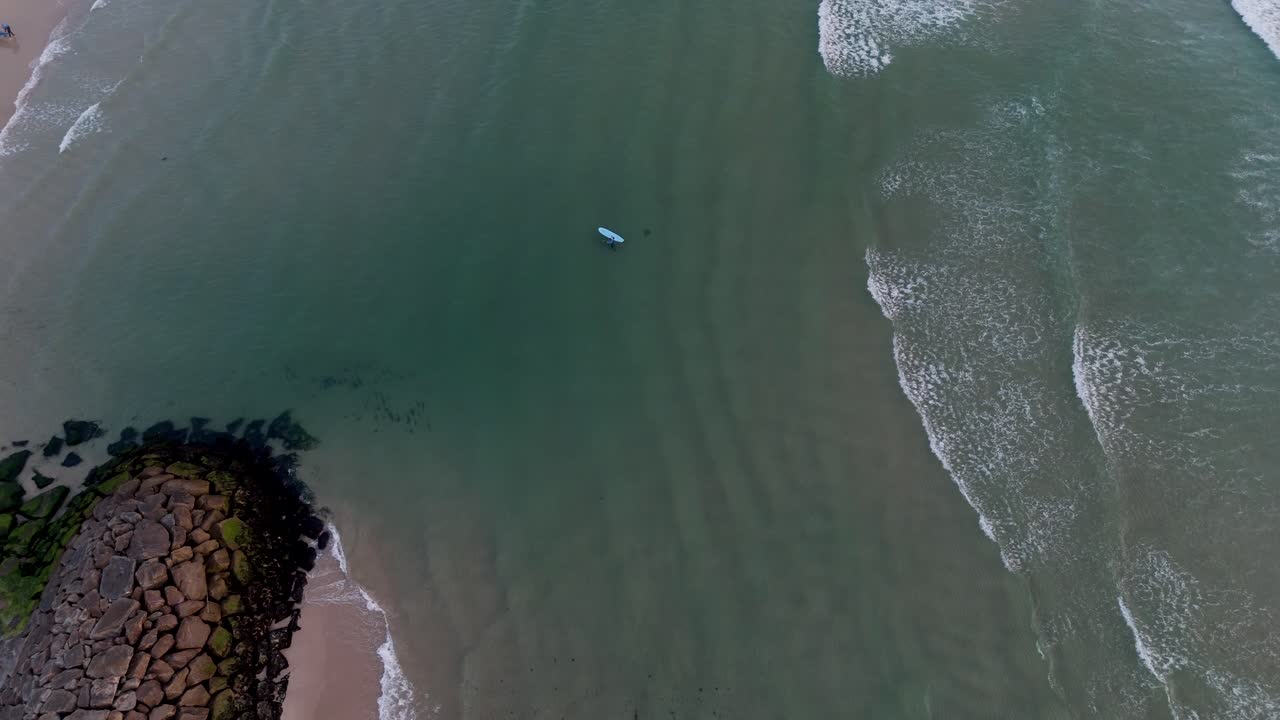 포르투갈 상페드로 오바르의 마세다 해변에서 바위 방파제 옆에서 파도를 타는 서퍼의 항공 촬영
