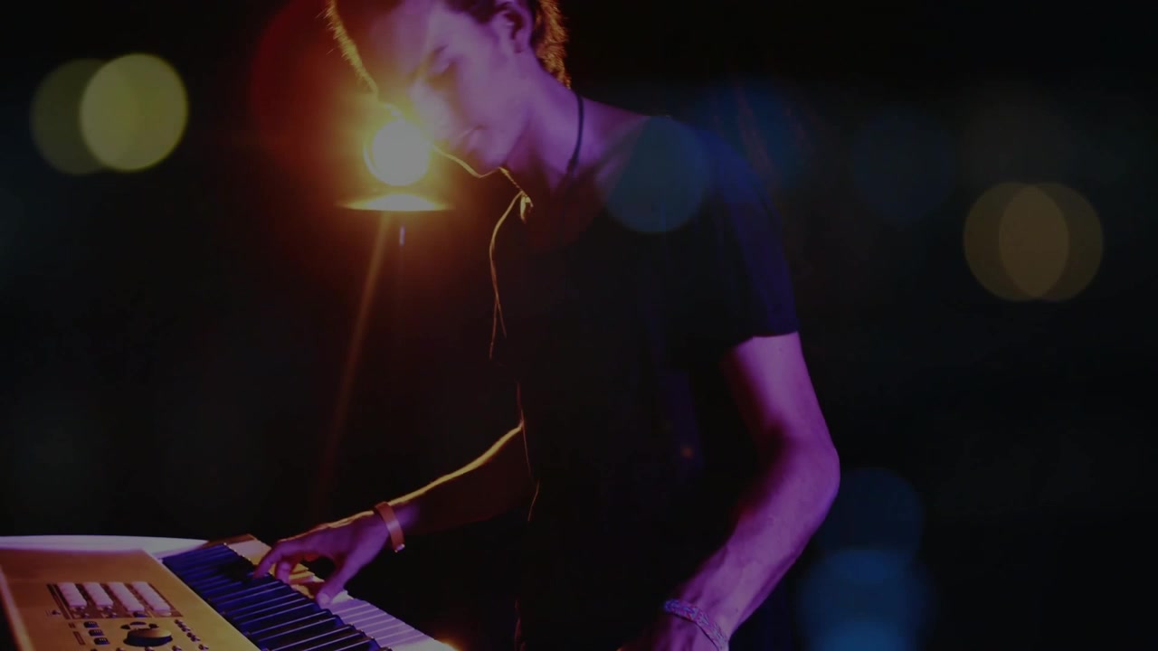 Musiker, der trykker på tangenter og flytter hænderne, mens han/hun skaber ambient synthmusik med varm lampebokeh.