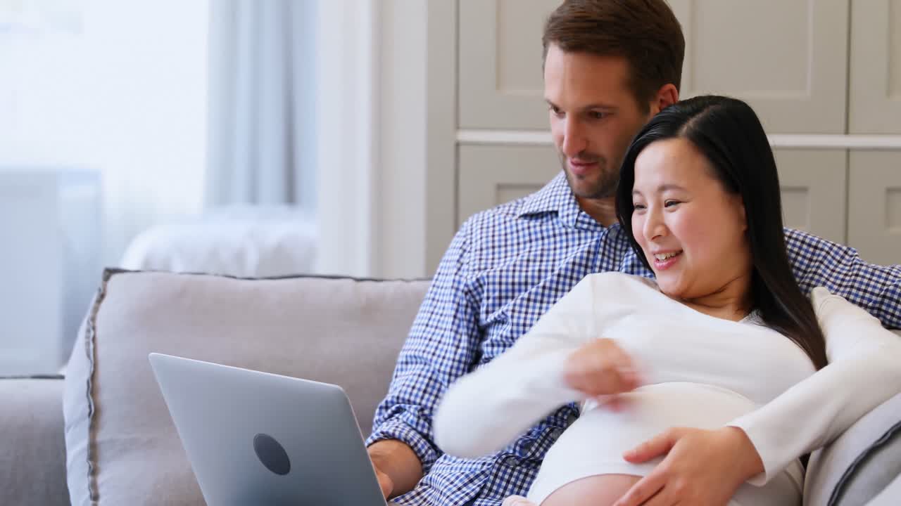 Pregnant couple using laptop on bed in living room 4k