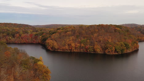 disparo de un camión aéreo, dejado sobre el embalse, mientras la cámara del dron se enfoca en las copas de los árboles de color naranja del otoño - montañas en un día nublado de otoño en la nueva presa de croton en el condado de westchester, ny