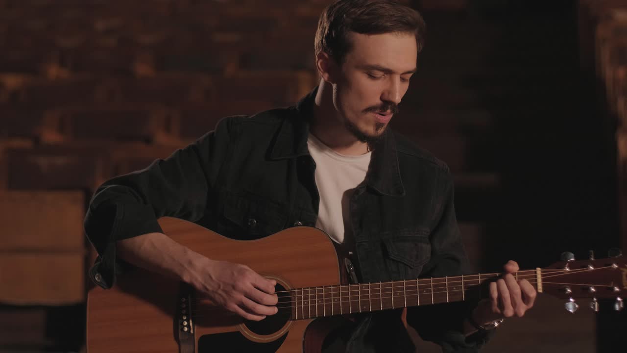 un chico guapo toca una guitarra acústica en un cine abandonado. el músico canta una canción y acompaña en la guitarra
