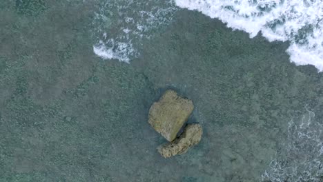 Top-Down-Slow-Motion-Drone-View-of-Waves-crashing-over-shallow-coral-reef-and-big-rock-in-Uluwatu-Bali-Indonesia