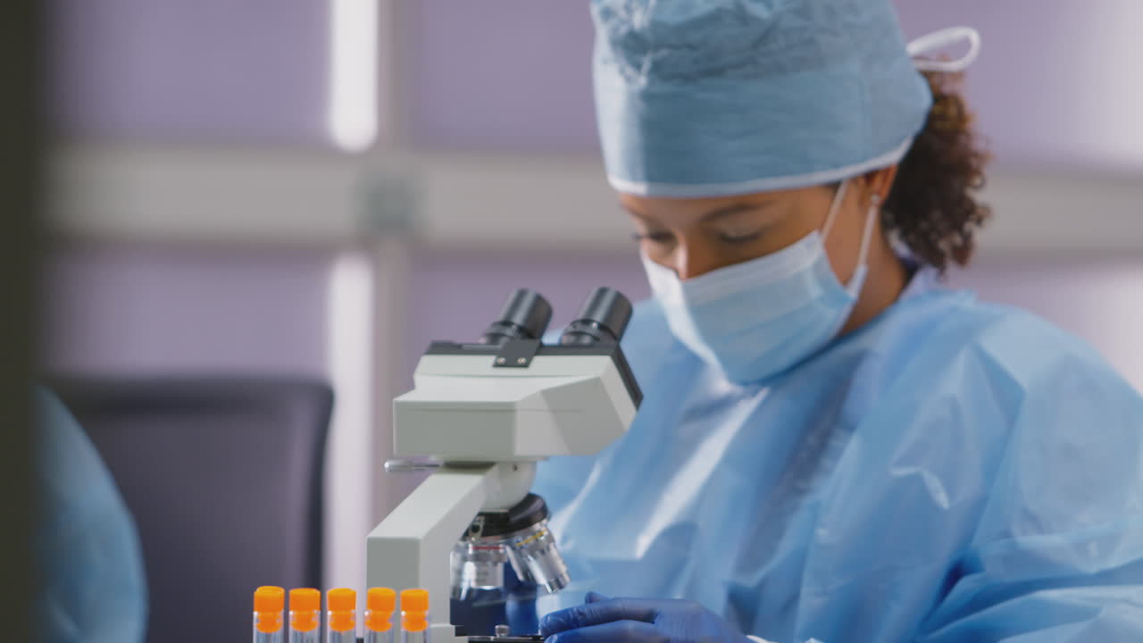 Female Lab Worker Wearing PPE Analysing Slide Under Microscope